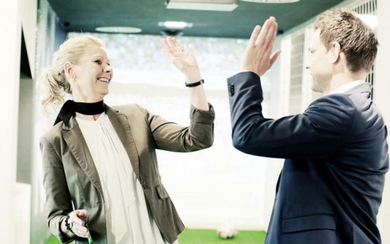 Symbolbild für Teambuilding in der Volkswagen Area - ein Mann im Anzug und eine Frau im Blazer geben sich ein High-Five.