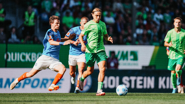 VfL-Wolfsburg-Spieler Lovro Majer führt den Ball und wird von einem Kieler-Gegenspieler bedrängt.