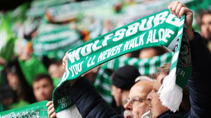 Fans vom VfL Wolfsburg halten eine Schal nach oben.
