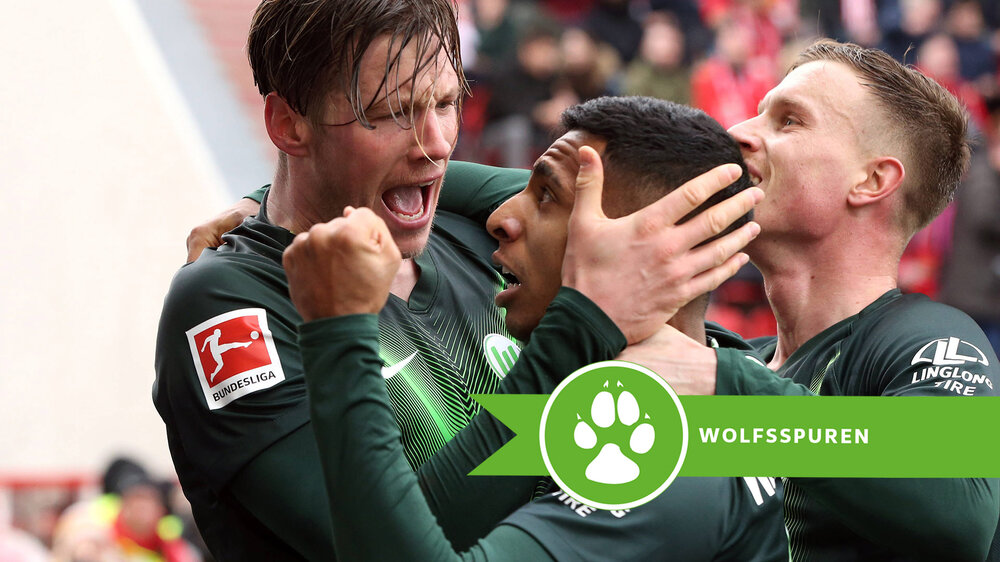 Der VfL-Wolfsburg-Spieler Wout Weghorst feiert ein Tor mit seinen Mitspielern. Auf der rechten Seite ist das Logo der Wolfsspuren zu sehen.