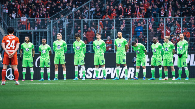 Die Spieler des VfL Wolfsburg stehen in Reihe bei einer Schweigeminute.