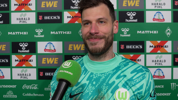 VfL-Wolfsburg-Torwart Marius Müller lacht vor einer Sponsorenwand.