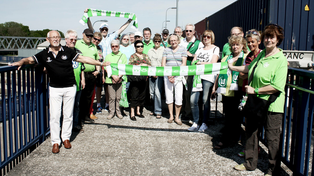 Gruppenbild von Mitgliedern des VfL Wolfsburg Wölfeclubs mit Schals bei einem Auswärtsspiel.