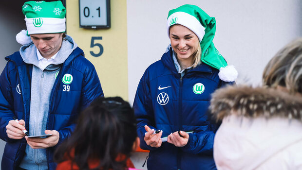 Die VfL Wolfsburg-Spielerin Jule Brand und Patrick Wimmer schreiben lachend Autogramme.