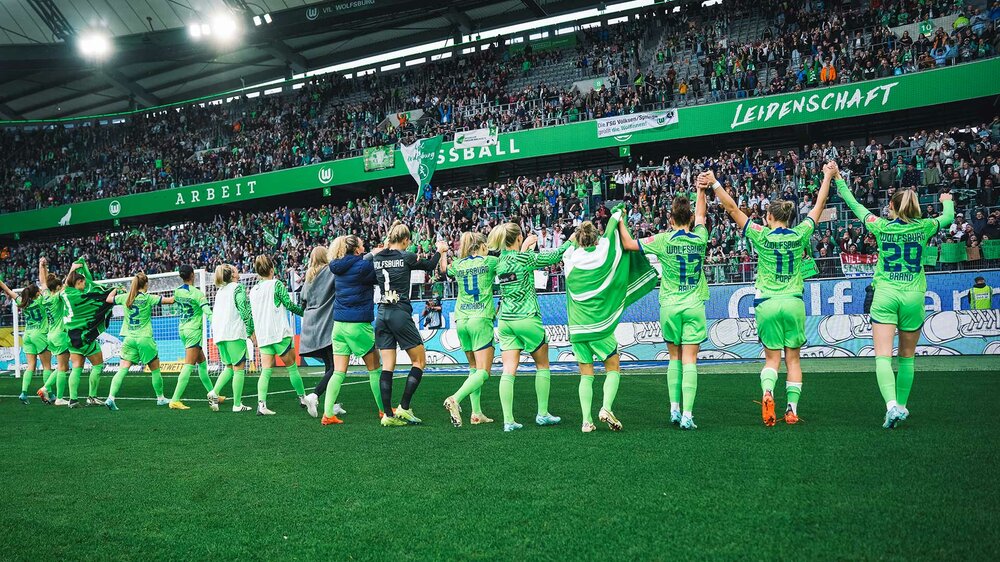 Die Spielerinnen des VfL Wolfsburg stehen vor der Fankurve und jubeln.