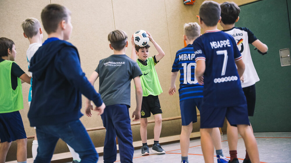 Jungen spielen im Rahmen der Schul-AG des VfL-Wolfsburg in einer Turnhalle Fußball.