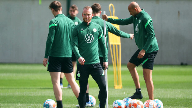 Maximilian Arnold schaut im Trainingsdress in die Kamera, hinter ihm sind Brooks, Philipp und weitere Wölfe mit Bällen zugange beim Training des VfL Wolfsburg an der Volkswagen Arena.