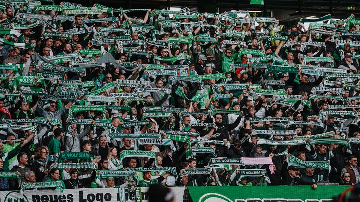 Fans des VfL Wolfsburg die in der Nordkurve ihre Schals nach oben halten.