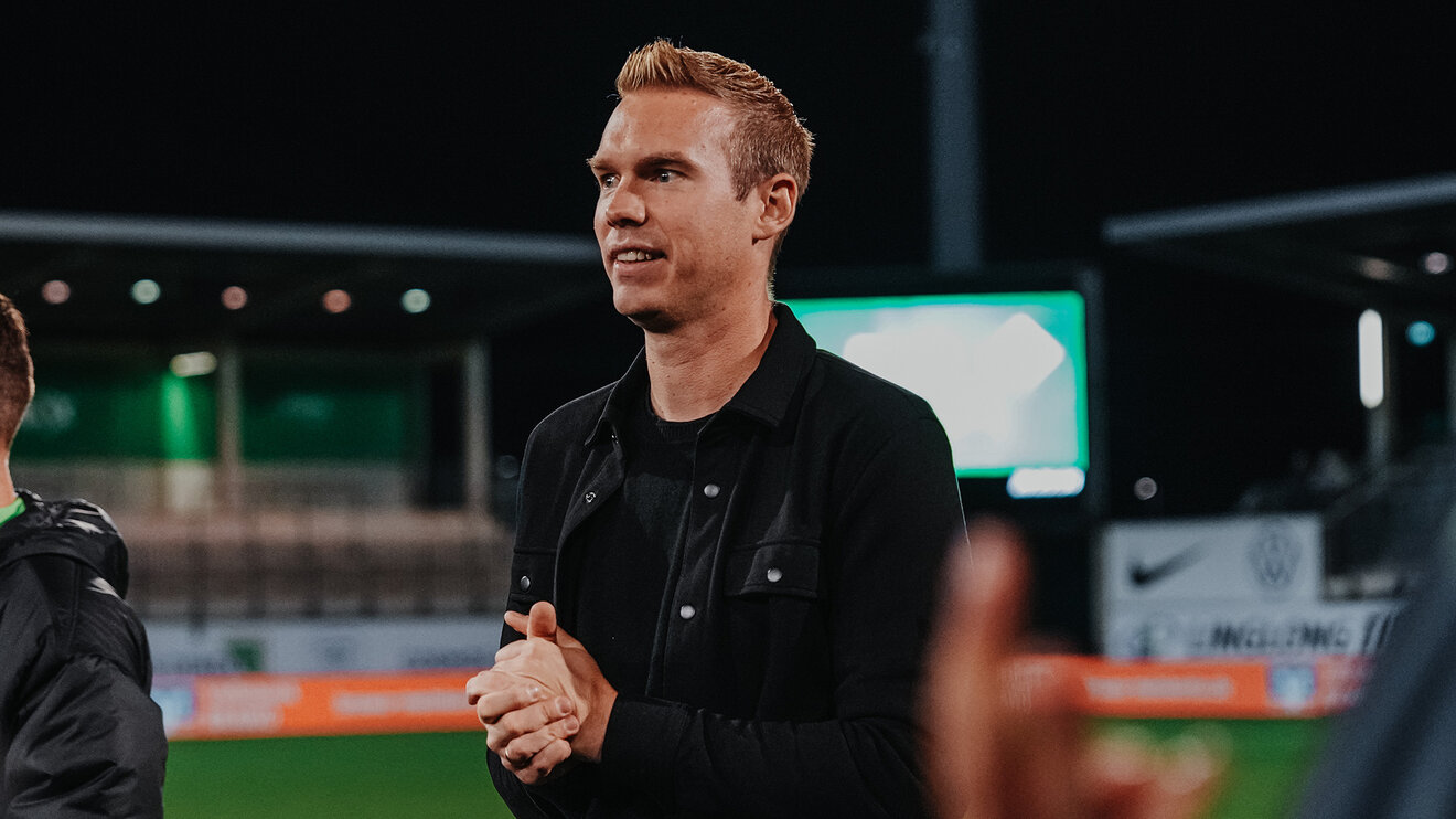 VfL-Frauen-Trainer Tommy Stroot faltet seine Hände vor sich und lächelt.