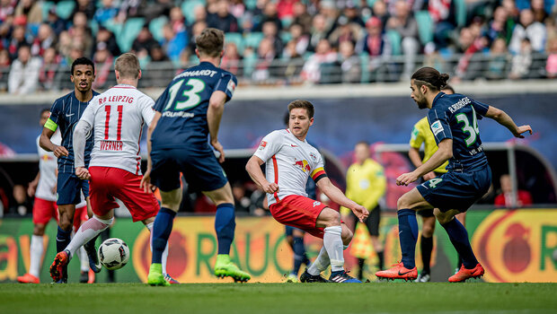 Am Ball ein Spieler vom RB Leipzig. Vor ihm ein weiterer Mitspieler dem er gerade den Ball zuspielen will. Um ihn herum sind drei Spieler des VfL-Wolfsburg.