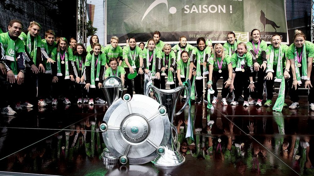 Die Frauen des VfL Wolfsburg. Die Frauen des VfL Wolfsburg stehen um Champions League Pokal, DFB Pokal und Meisterschale.