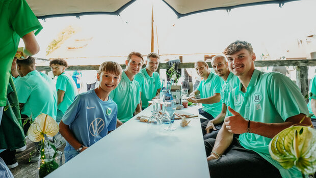 Die Spieler des VfL Wolfsburg sitzen an der Tafel und lächeln in die Kamera.