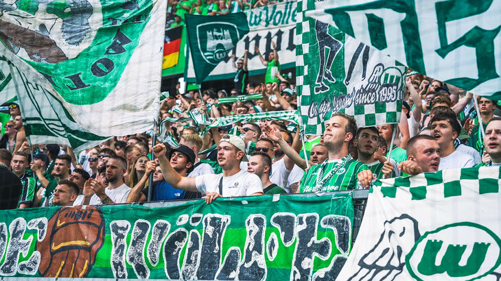 Fans des VfL Wolfsburg feuern mit Fahnen und Schals die Männer-Mannschaft an.