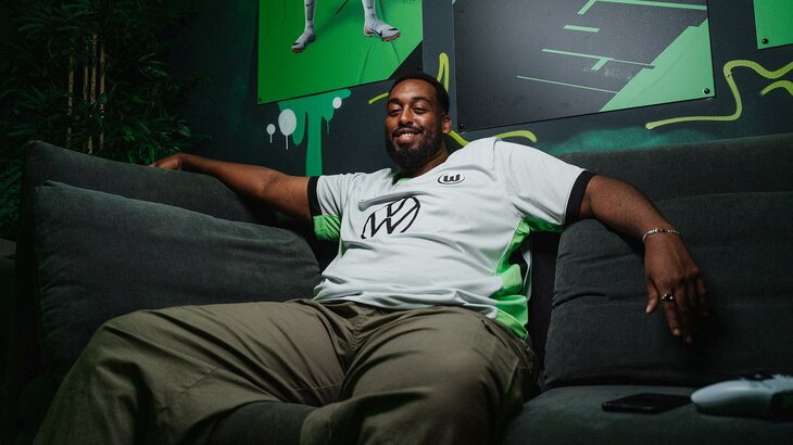 VfL-Wolfsburg-E-Sport-Content-Creator Abdallah „Faro“ Farah sitzt auf einem Sofa und lächelt.