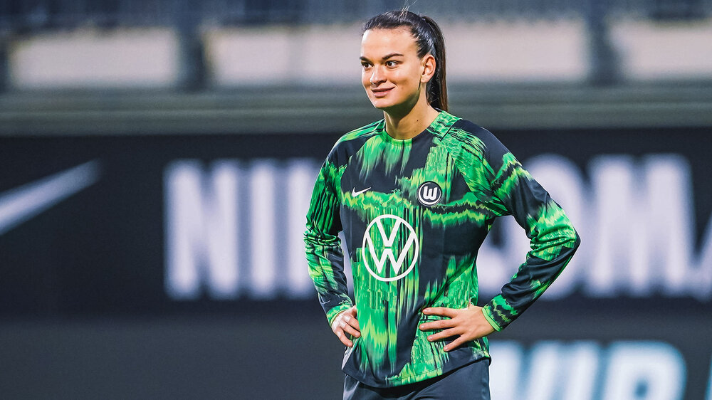 VfL-Wolfsburg-Spielerin Riola Xhemaili stemmt ihre Hände in die Hüfte und lacht.