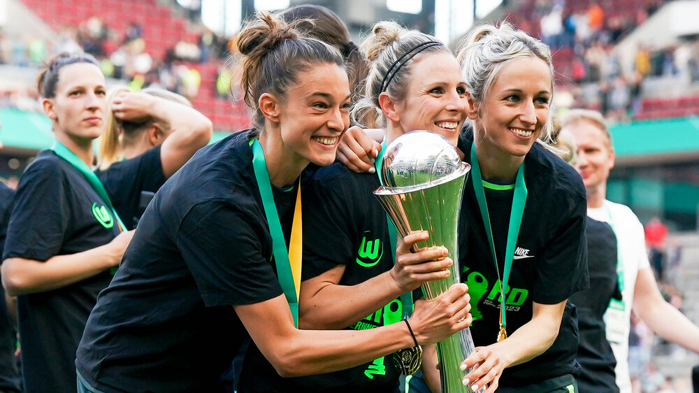 Felicitas Rauch vom VfL Wolfsburg hält mit ihren Teamkolleginnen die DFB-Pokal-Trophäe in der Hand und lächelt.