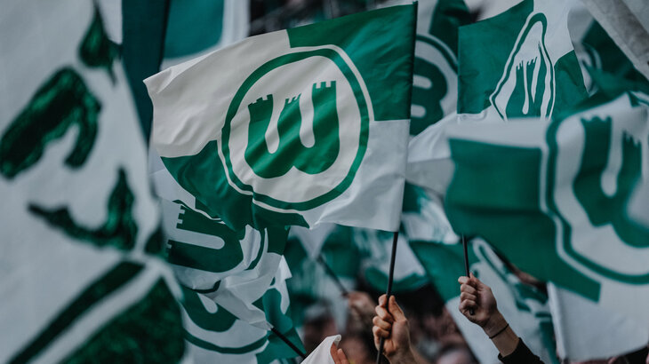 Fans des VfL Wolfsburg schwenken grün-weiße Fahnen.