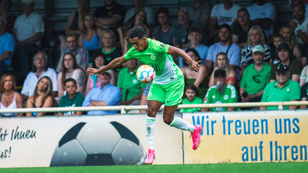Ein Spieler des VfL Wolfsburg springt in die Luft und nimmt einen Ball an.