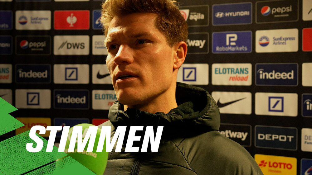 VfL-Wolfsburg-Spieler Kevin Behrens am Mikrofon. Daneben ist der Schriftzug “Stimmen”. 