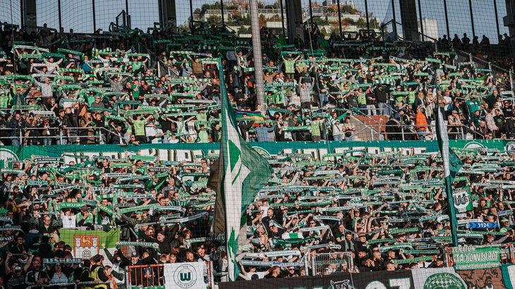 Die VfL-Wolfsburg-Fans im Fanblock halten alle einen Schal nach oben.