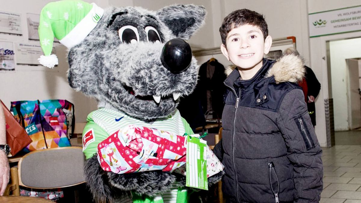 Wölfi hat ein Kind im Arm bei der Weihnachtswunschaktion vom VfL Wolfsburg.