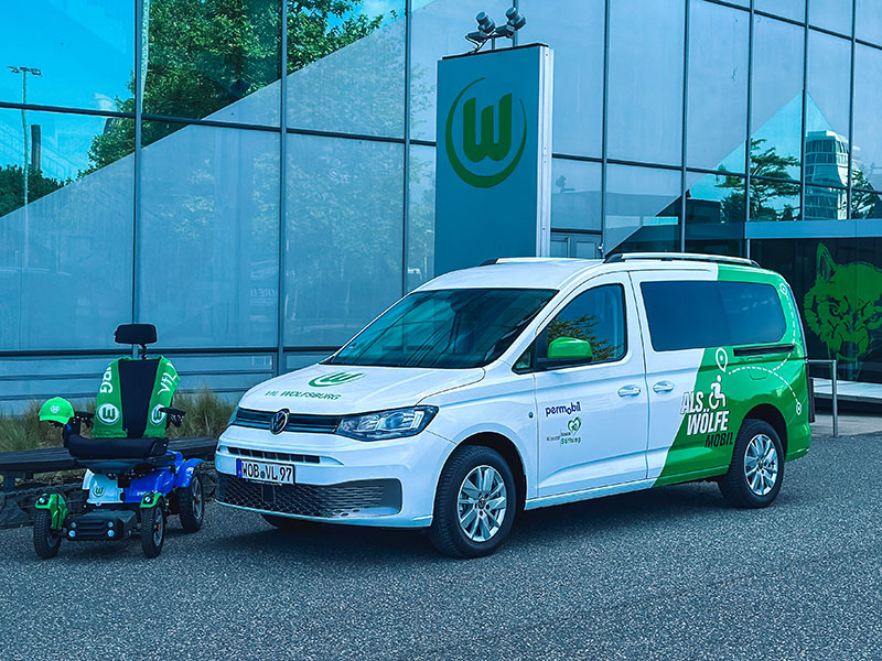 Das ALS-Mobil sowie der E-Rollstuhl des VfL Woflsburg stehen vor der Volkswagen Arena.