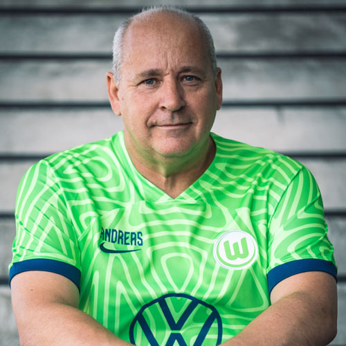 Der Fanbeauftragte Andreas sitzt im VfL Wolfsburg-Trikot auf einer Treppe.