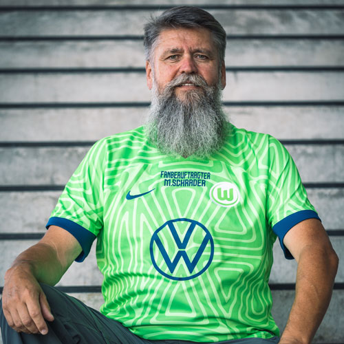 Der Fanbeauftragte Michael Schrader sitzt im VfL Wolfsburg-Trikot auf einer Treppe.