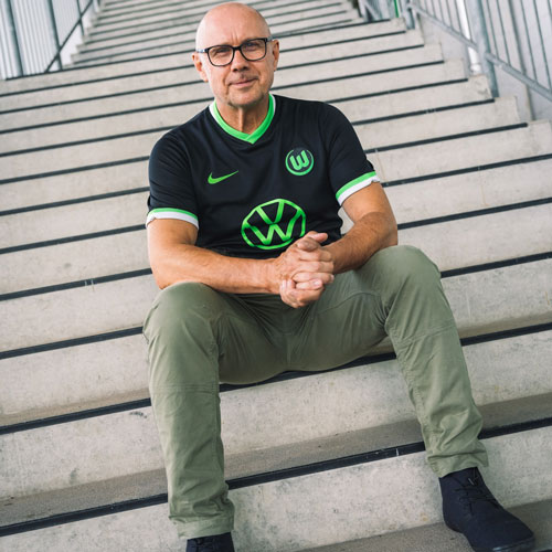 Der Fanbeauftragte Carsten sitzt im VfL Wolfsburg-Trikot auf einer Treppe.
