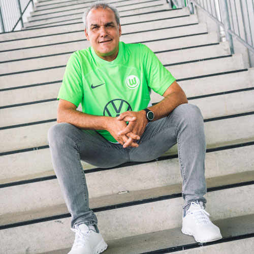 Der Fanbeauftragte Holger sitzt im VfL Wolfsburg-Trikot auf einer Treppe.