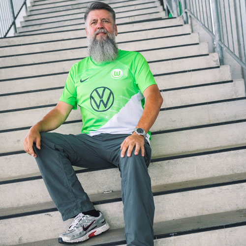 Der Fanbeauftragte Michael sitzt im VfL Wolfsburg-Trikot auf einer Treppe.