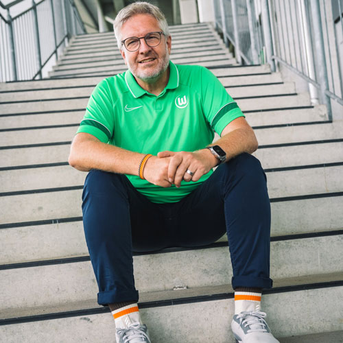 Der Fanbeauftragte Peter sitzt im VfL Wolfsburg-Trikot auf einer Treppe.