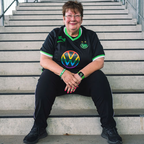Die Fanbeauftragte Petra sitzt im VfL Wolfsburg-Trikot auf einer Treppe.