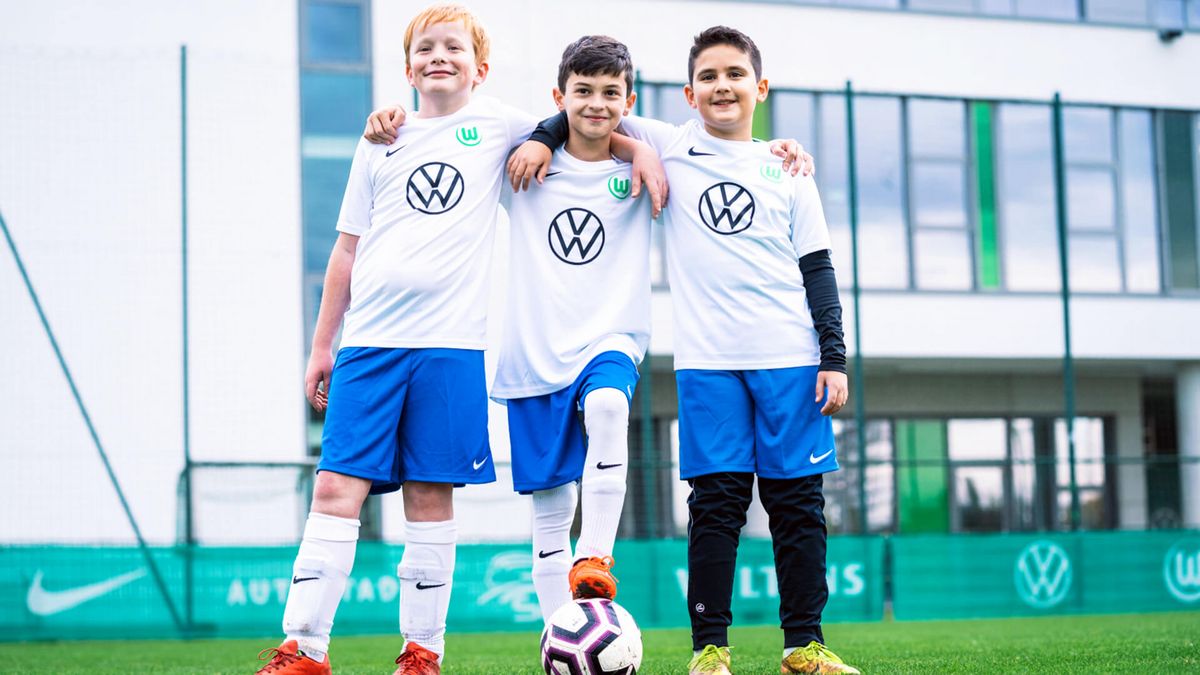 Drei Kinder der VfL Wolfsburg-Fußballschule halten sich im Arm.