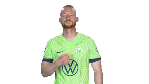 Der VfL Wolfsburg-Spieler Maximilian Arnold zeigt auf das Logo.