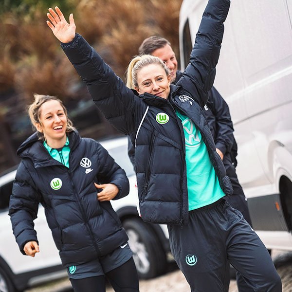 VfL Wolfsburg Spielerin Blomqvist ist mit Winterjacke bekleidet auf dem Weg zum Training und streckt in die Kamera lachend die Arme nach oben.
