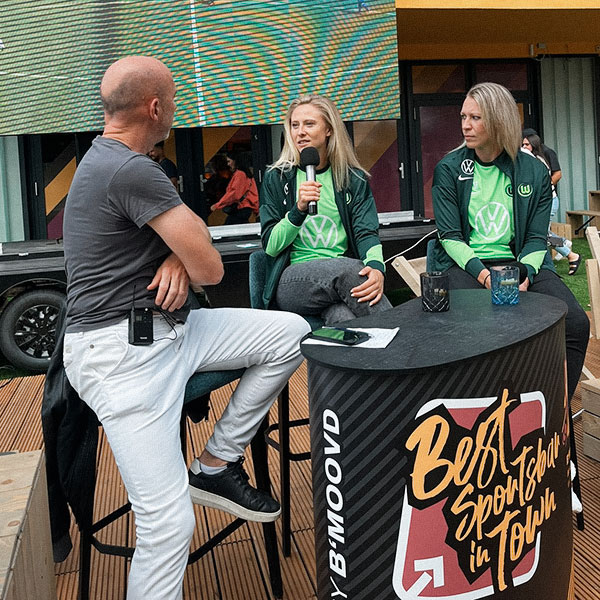 VfL-Wolfsburg-Spielerinnen Rebecka Blomqvist und Kristin Demann sitzen neben einem Mann und geben ein Interview.