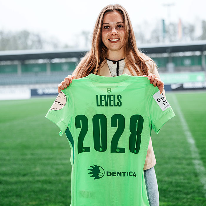 Die neue Wolfsburg Spielerin Janou Levels steht im AOK Stadion und hält ein Trikot mit der Rückennummer 2028 in die Kamera.
